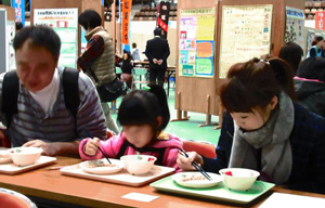 親子で真剣。給食まつり恒例の「おはしで豆つかみ！」の画像